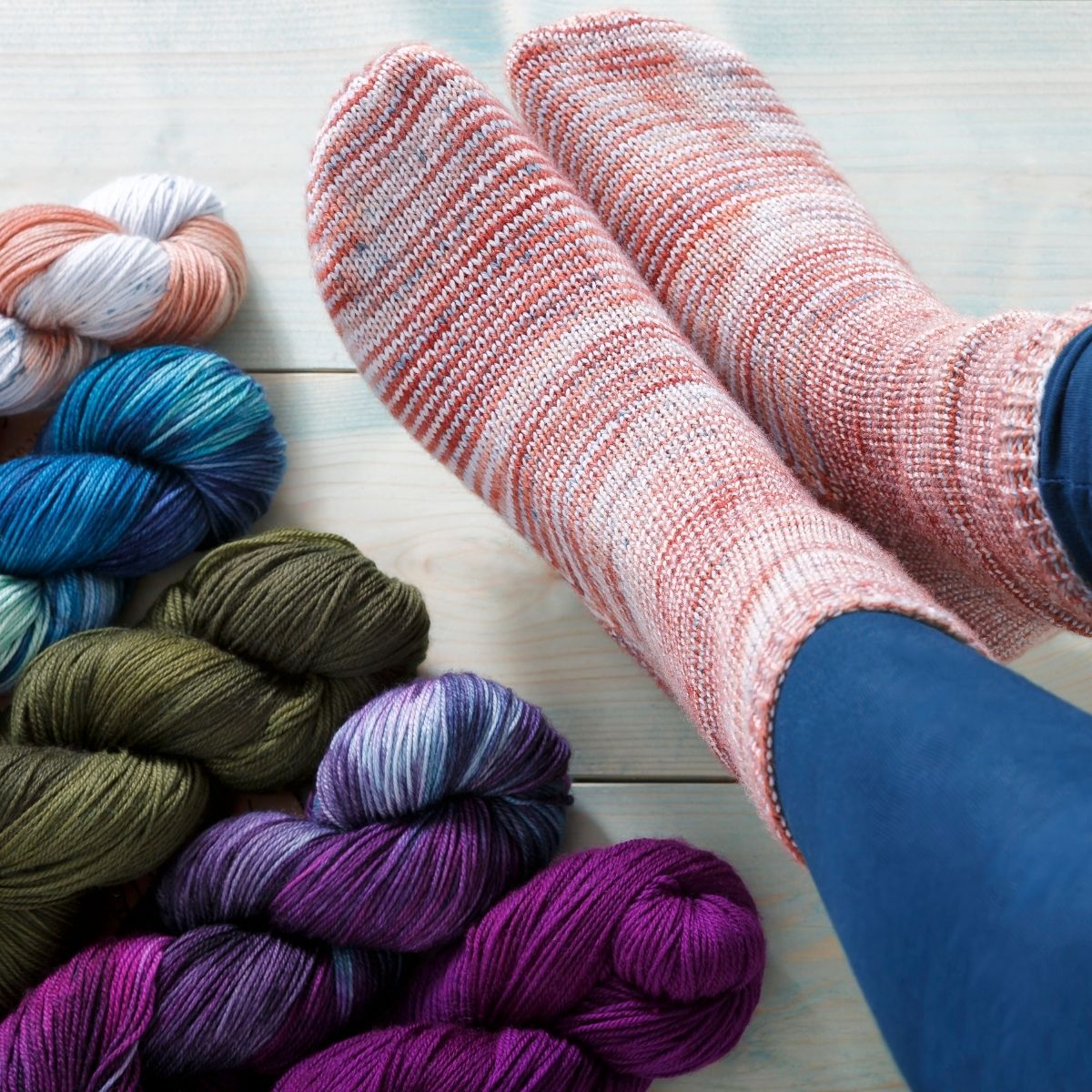A woman's feet  are pictured, wearing hand knit socks in Manos del Uruguay Alegria. The colorway of the socks is Colorado river, additional skeins of yarn are shown.