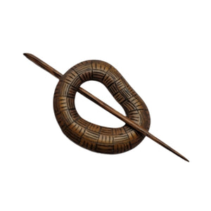 A bronze colored wooden shawl pin in shown, etched with basketweave lines.