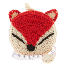 Load image into Gallery viewer, A crochet covered tape measure in the shape of a fox head with a red-orange and white face, with black nose and eyes.

