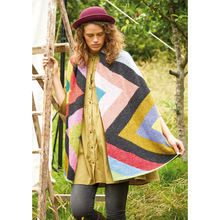 Load image into Gallery viewer, A woman in a felted hat stands by a ladder in dark jeans and a mustard colored tunic and displays the wrap she is wearing which features an exaggeratedly wide, colorful zig zag pattern along its length.
