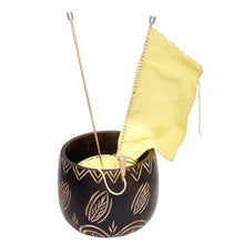 Load image into Gallery viewer, A wooden yarn bowl is shown in black with etched leaf designs that allow the natural wood color to show through. Inside are two knitting needles with a knitted rectangle and ball of yellow yarn.
