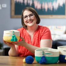 Load image into Gallery viewer, Linda Permann is shown holding a yellow basket with green tassels, as well as the two other baskets in the crocheted set.
