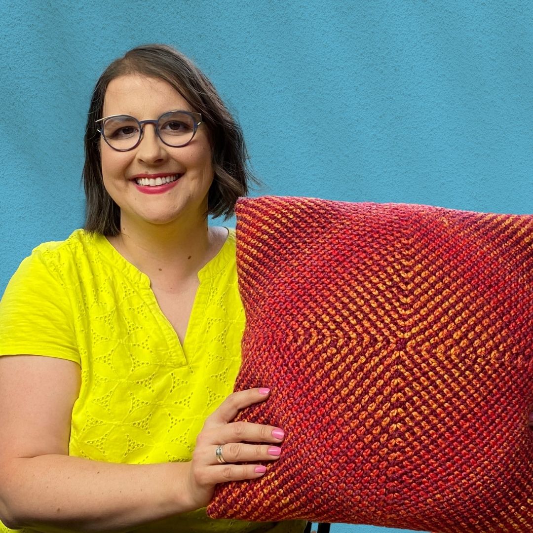 Linda Permann is shown holding an orange crochet pillow with a gradient color effect.