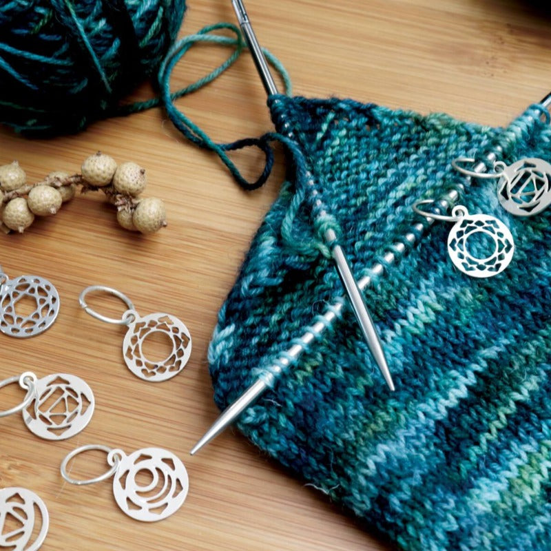 Sterling silver Mindful  chakra stitch markers are shown in use on a project featuring blue and green yarn.