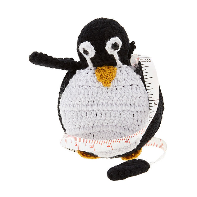 A crochet covered tape measure in the shape of a black and white penquin with a yellow beak and feet.
