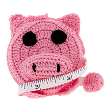 Load image into Gallery viewer, A crochet covered tape measure in the shape of a pig&#39;s face, featuring a pink face and black features.
