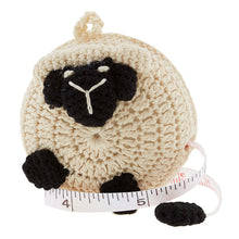 Load image into Gallery viewer, A crochet covered tape measure in the shape of a sheep with white wool and black face and feet.
